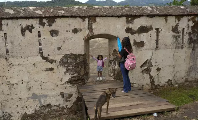 A woman takes a photo of her daughter at the San Jeronimo fort in Portobelo, Panama, Monday, Oct. 21, 2024, during a festival celebrating the iconic Black Christ statue that was found on the shore in 1658. (AP Photo/Matias Delacroix)