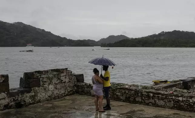 People stand under an umbrella at the San Jeronimo fort in Portobelo, Panama, Sunday, Oct. 20, 2024, a day before the Black Christ festival. (AP Photo/Matias Delacroix)