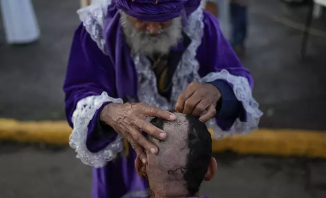 Barber Jose Valdespinto cuts a pilgrim's hair, part of the pilgrim's penance, outside the San Felipe Church to honor the Black Christ in Portobelo, Panama, Monday, Oct. 21, 2024, during a festival celebrating the iconic statue that was found on the shore in 1658. (AP Photo/Matias Delacroix)