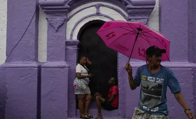 People take cover from rain at San Felipe Church in Portobelo, Panama, Sunday, Oct. 20, 2024, a day before the Black Christ festival. (AP Photo/Matias Delacroix)