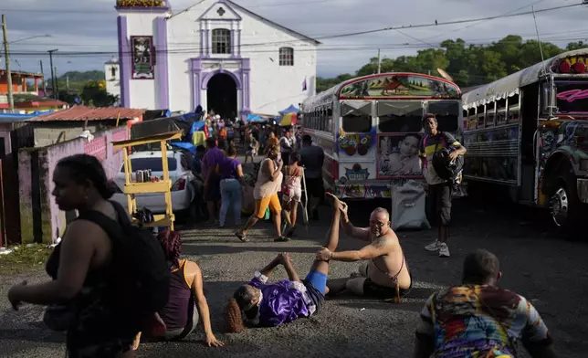 Pilgrim Ernesto Troya stretches his friend's leg as they take a break from crawling on their knees to San Felipe Church, behind, to honor the Black Christ in Portobelo, Panama, Monday, Oct. 21, 2024, during a festival celebrating the iconic statue that was found on the shore in 1658. (AP Photo/Matias Delacroix)