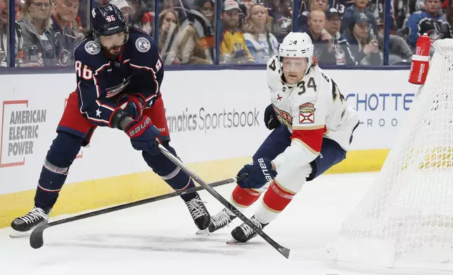 Columbus Blue Jackets' Kirill Marchenko, left, passes the puck past Florida Panthers' Adam Boqvist during the second period of an NHL hockey game Tuesday, Oct. 15, 2024, in Columbus, Ohio. (AP Photo/Jay LaPrete)