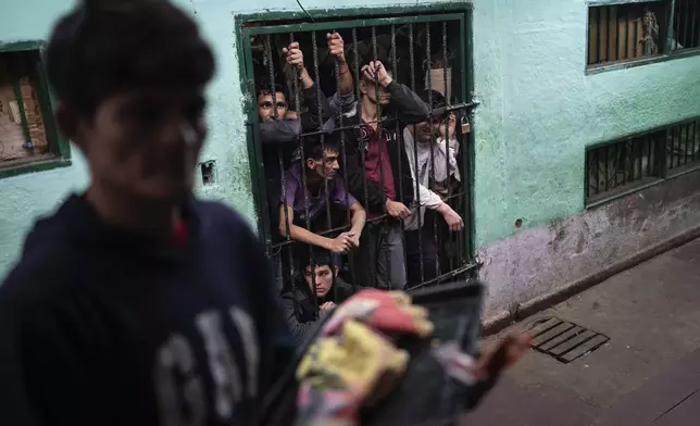 Prisoners peer from their group cell in the late afternoon, to be unlocked in the morning, as another prisoner prepares to enter another group cell to be locked for the night at the Regional Penitentiary in Villarica, Paraguay, Saturday, Aug. 31, 2024. (AP Photo/Rodrigo Abd)