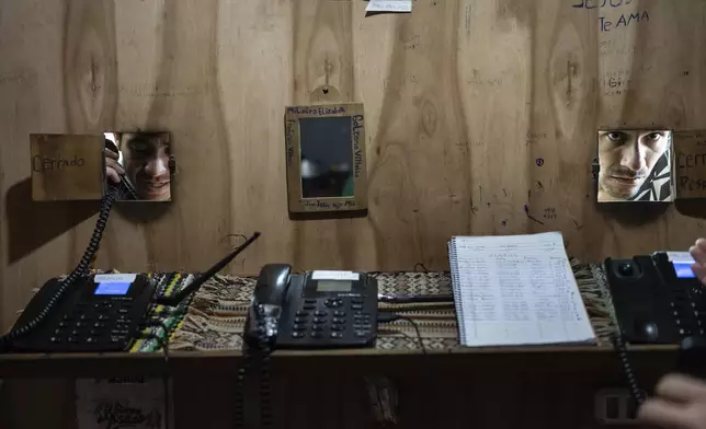 An inmate uses a phone as another gives the number to dial at a pay-by-the-minute phone booth set up and run by prisoners at the Regional Penitentiary in Villarica, Paraguay, Sunday, Sept. 1, 2024. Most inmates' calls get paid for by their families when they come to visit in person. (AP Photo/Rodrigo Abd)