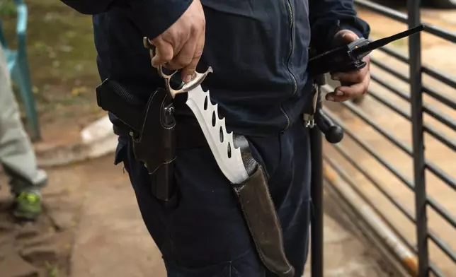 A prison security guard shows the knife he carries as he patrols outside the Regional Penitentiary in Villarica, Paraguay, Saturday, Aug. 31, 2024. (AP Photo/Rodrigo Abd)