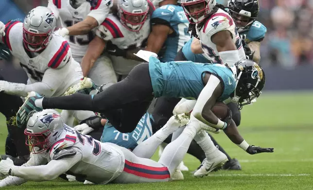 Jacksonville Jaguars running back D'Ernest Johnson (2) falls over New England Patriots linebacker Anfernee Jennings (33) during the second half of an NFL football game, Sunday, Oct. 20, 2024, in London. (AP Photo/Kin Cheung)