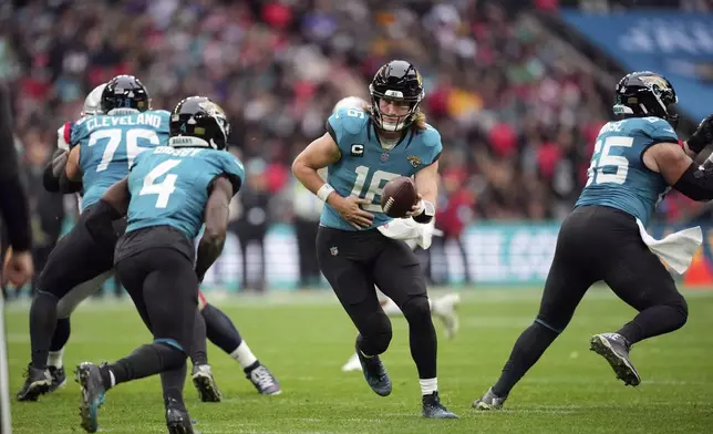 Jacksonville Jaguars quarterback Trevor Lawrence (16) hands off to running back Tank Bigsby (4) during the first half of an NFL football game against the New England Patriots, Sunday, Oct. 20, 2024, in London. (AP Photo/Kin Cheung)