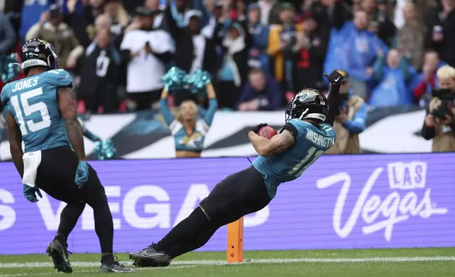 Teammates cheer as Jacksonville Jaguars' Parker Washington (11) falls into the endzone for a 96-yard touchdown on a punt return during the first half of an NFL football game against the New England Patriots, Sunday, Oct. 20, 2024, in London. (AP Photo/Ian Walton)