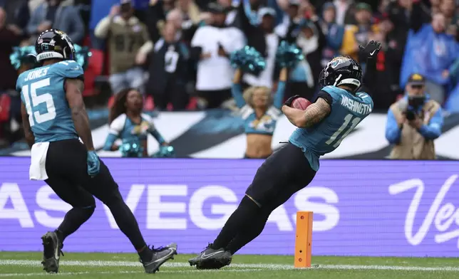 Teammates cheer as Jacksonville Jaguars' Parker Washington (11) falls into the endzone for a 96-yard touchdown on a punt return during the first half of an NFL football game against the New England Patriots, Sunday, Oct. 20, 2024, in London. (AP Photo/Ian Walton)