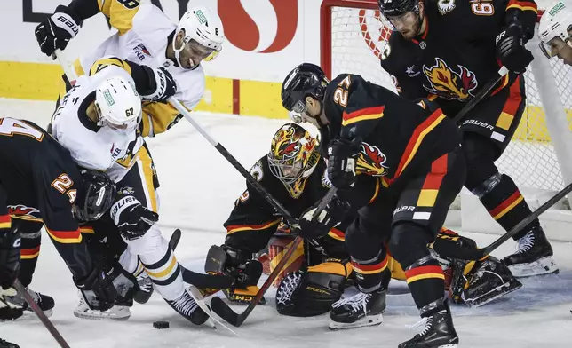 Pittsburgh Penguins' Rickard Rakell, second left, and Michael Bunting, third left, struggle to get at the puck as Calgary Flames goalie Dustin Wolf, center, and Matthew Coronato, center right, try to clear it as Daniil Miromanov, right, looks on during the first period of an NHL hockey game on Tuesday, Oct. 22, 2024 in Calgary, Alberta. (Jeff McIntosh/The Canadian Press via AP)