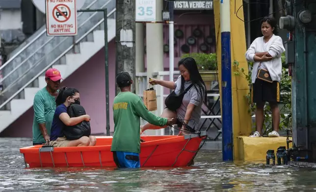 Residents use a boat to cross flooded streets caused by Tropical Storm Trami on Friday, Oct. 25, 2024, in Cainta, Rizal province, Philippines. (AP Photo/Aaron Favila)