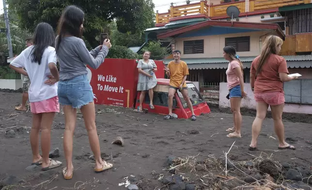 Residents pose beside a delivery van buried by volcanic mud that flowed down from Mayon volcano after heavy rains caused by Tropical Storm Trami hit Guinobatan town, Albay province, Philippines on Wednesday Oct. 23, 2024. (AP Photo/John Michael Magdasoc)