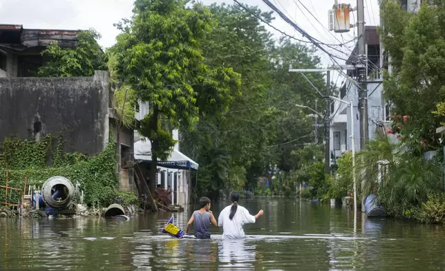 Residents walk along the flooded village caused by Tropical Storm Trami on Friday, Oct. 25, 2024, in Cainta, Rizal province, Philippines. (AP Photo/Aaron Favila)