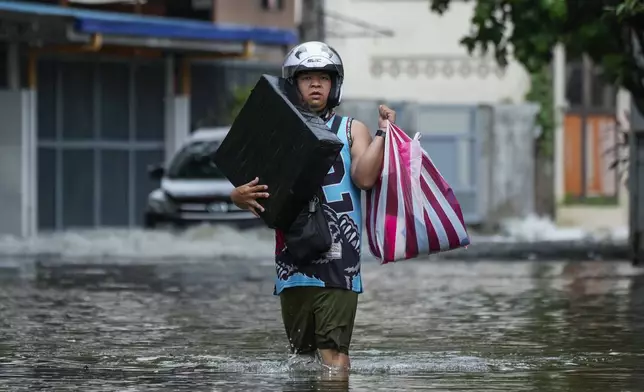 A resident carries belongings as he crosses flooded streets caused by Tropical Storm Trami on Friday, Oct. 25, 2024, in Cainta, Rizal province, Philippines. (AP Photo/Aaron Favila)