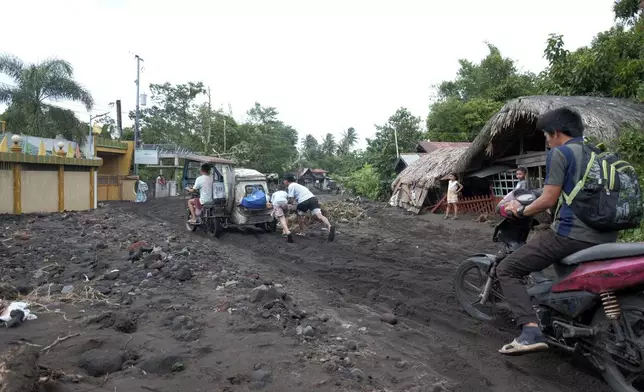 Residents negotiate a road covered with volcanic mud that flowed down from Mayon volcano after heavy rains caused by Tropical Storm Trami hit Guinobatan town, Albay province, Philippines on Wednesday Oct. 23, 2024. (AP Photo/John Michael Magdasoc)