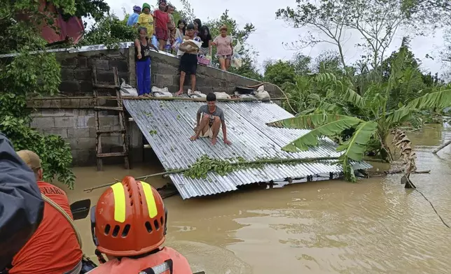 In this photo provided by the Philippine Coast Guard, residents staying on top of their roofs to avoid floods caused by Tropical Storm Trami, locally named Kristine, await to be rescued at Libon, Albay province, Philippines on Wednesday Oct. 23, 2024. (Philippine Coast Guard via AP)