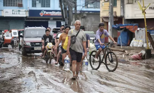 Residents walk along a muddied road as they start cleaning their area after floods caused by Tropical Trami, locally named Kristine, in Polangui, Albay province, Philippines on Oct. 23, 2024. (AP Photo/John Michael Magdasoc)