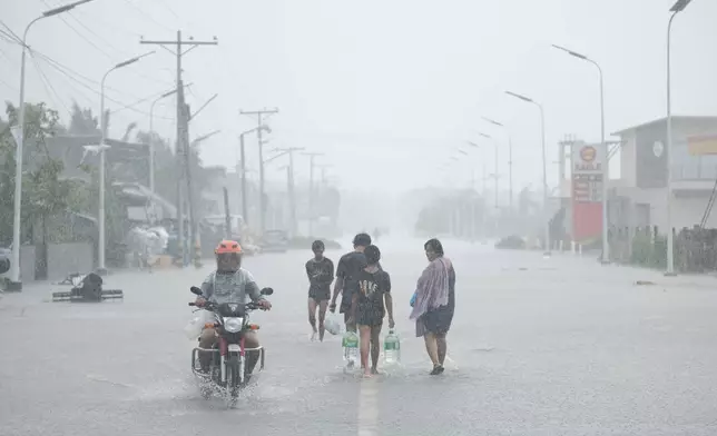 Residents carry drinking water along a flooded road as rains continue on Thursday Oct. 24, 2024 after Tropical Storm Trami, locally named Kristine, caused heavy flooding at Libon town, Albay province, Philippines. (AP Photo/John Michael Magdasoc)