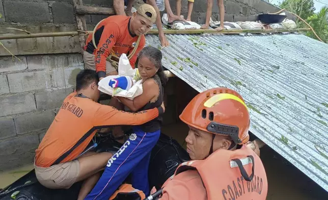 In this photo provided by the Philippine Coast Guard, a resident carries a baby as they are rescued from their roofs where they were staying to avoid floods caused by Tropical Storm Trami, locally named Kristine, at Libon, Albay province, Philippines on Wednesday Oct. 23, 2024. (Philippine Coast Guard via AP)