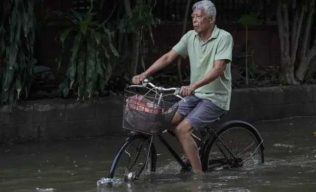 A resident rides his bike as he crosses flooded streets caused by Tropical Storm Trami on Friday, Oct. 25, 2024, in Cainta, Rizal province, Philippines. (AP Photo/Aaron Favila)