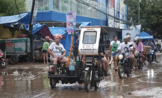 Residents pass by a muddied road after floods caused by Tropical Trami hit Polangui town, Albay province, Philippines Wednesday, Oct. 23, 2024. (AP Photo/John Michael Magdasoc)