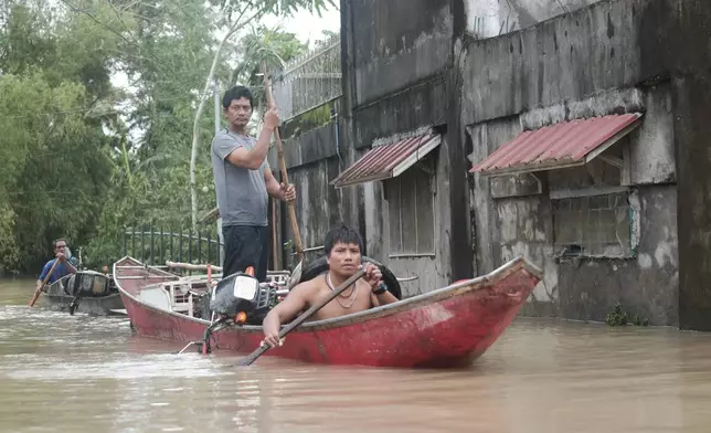 Residents use a boat to recover items from their flooded homes caused by Tropical Storm Trami, locally named Kristine, as it continues to inundate Libon town, Albay province, Philippines on Thursday Oct. 24, 2024. (AP Photo/John Michael Magdasoc)