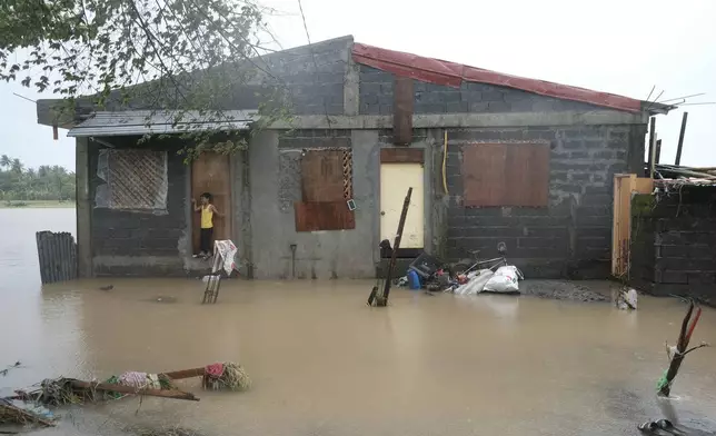 A boy stands outside a flooded house on Thursday Oct. 24, 2024, after Tropical Storm Trami, locally named Kristine, dumped heavy rains at Libon town, Albay province, Philippines. (AP Photo/John Michael Magdasoc)