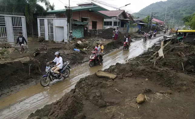 Residents ride motorcycles along a mud covered road after a landslide triggered by Tropical Storm Trami, recently struck Talisay, Batangas province, Philippines, Saturday, Oct. 26, 2024 . (AP Photo/Aaron Favila)