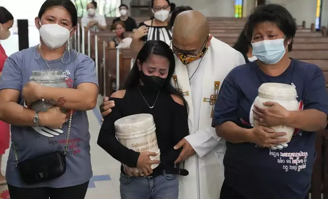 FILE - Catholic priest Flaviano "Flavie" Villanueva comforts relatives as they receive the urns containing the remains of victims of alleged extrajudicial killings of President Rodrigo Duterte's so-called war on drugs at a church in Quezon city, Philippines, Wednesday, Sept. 28, 2022. (AP Photo/Aaron Favila, File)