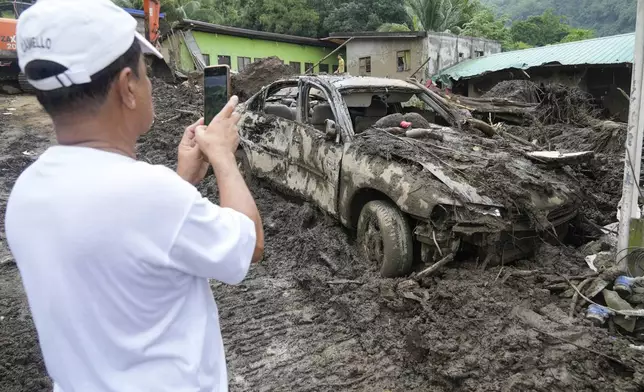 A villager takes a photo of a damaged car after a recent landslide triggered by Tropical Storm Trami struck Talisay, Batangas province, Philippines leaving thousands homeless and several villagers dead on Saturday, Oct. 26, 2024. (AP Photo/Aaron Favila)