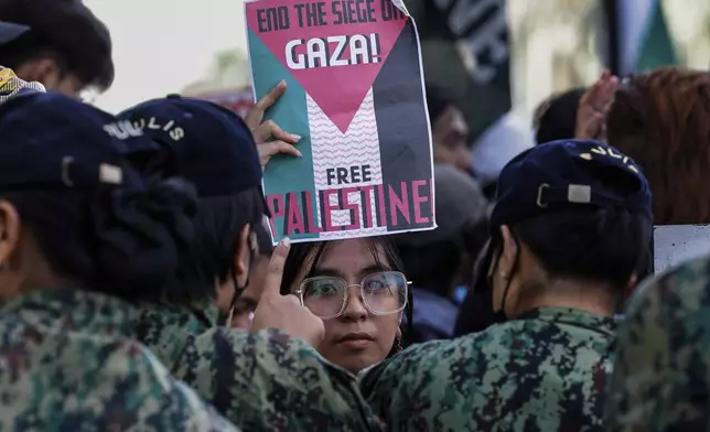 An activist raises a placard as police personnel block activists from marching near the U.S. Embassy in Manila on Saturday, Oct.5, 2024, as they hold a protest to observe the first-year anniversary of the war in Gaza.(AP Photo/Gerard V. Carreon)