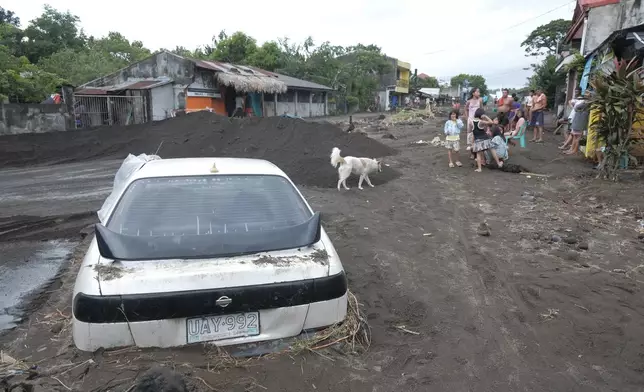 Residents stay beside a car partially buried by volcanic mud that had flowed down from Mayon volcano after heavy rains caused by Tropical Storm Trami hit Guinobatan town, Albay province, Philippines on Wednesday Oct. 23, 2024. (AP Photo/John Michael Magdasoc)