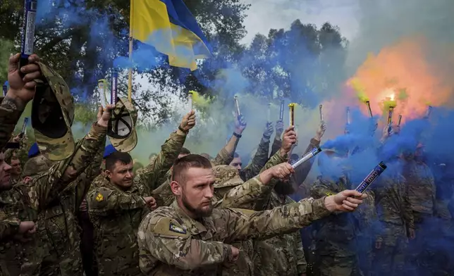 Ukrainian servicemen of the Azov brigade light flares during the funeral ceremony of fallen comrade Ihor Kusochek, in Travkine, Chernihiv region, Ukraine, Friday Oct. 4, 2024. (AP Photo/Evgeniy Maloletka)