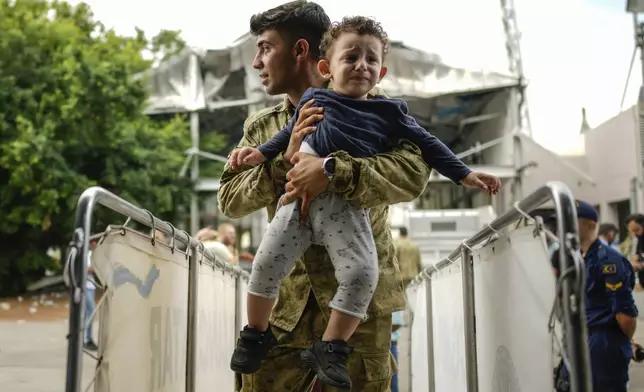 A Turkish military person carries a child on board of a Turkish military ship as he and hundreds of people, mostly Turkish citizens, are evacuated from Lebanon to Turkey, in Beirut port, on Thursday, Oct. 10, 2024. (AP Photo/Emrah Gurel)