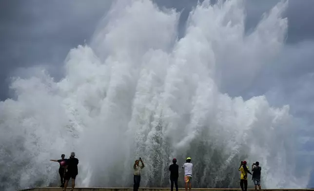 People take photos of the spray from waves crashing against the Malecon seawall, brought by the passing of Hurricane Milton in the Gulf of Mexico, in Havana, Cuba, Wednesday, Oct. 9, 2024. (AP Photo/Ramon Espinosa)