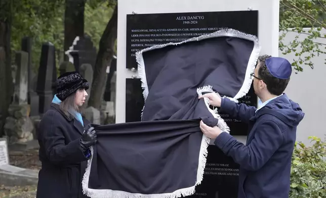 Yuval Danzig, right, the son of a Polish-Israeli man kidnapped and killed by Hamas, helps to unveil a plaque honoring his father, Alex Dancyg, in the Jewish cemetery in Warsaw, Poland, on Monday, Oct. 7, 2024. (AP Photo/Czarek Sokolowski)