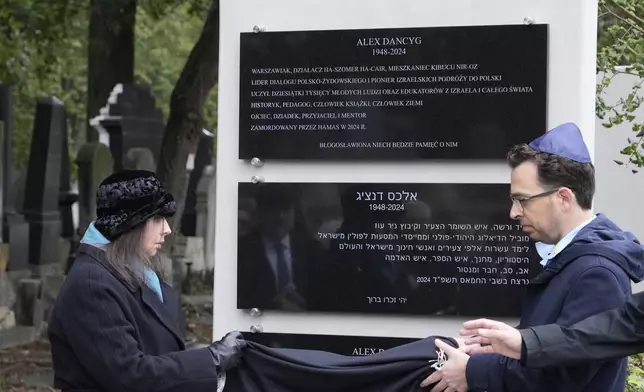 Yuval Danzig, right, the son of a Polish-Israeli man kidnapped and killed by Hamas, helps to unveil a plaque honoring his father, Alex Dancyg, in the Jewish cemetery on the one-year anniversary of the Hamas attack, in Warsaw, Poland, on Monday, Oct. 7, 2024. (AP Photo/Czarek Sokolowski)