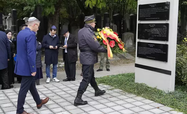 A wreath is brought to a plaque honoring Alex Dancyg, a Polish-Israeli man who was kidnapped by Hamas on Oct. 7, 2023, and later killed, in Warsaw's Jewish cemetery on the one-year anniversary of the Hamas attack, in Warsaw, Poland, on Monday, Oct. 7, 2024. (AP Photo/Czarek Sokolowski)