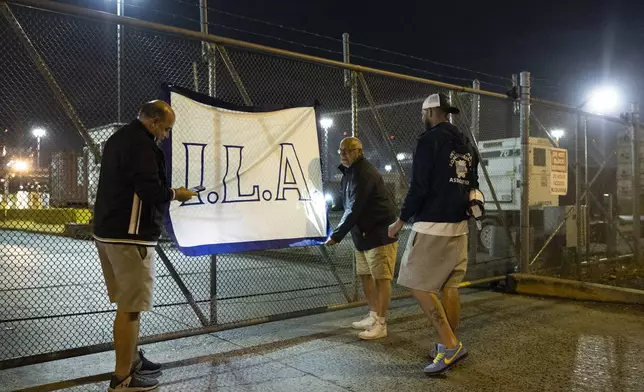 Philadelphia longshoremen hang the flag of the International Longshoremen's Association on a fence outside the Packer Avenue Marine Terminal Port, preparing to strike, as their contract runs out at midnight, Monday, Sept. 30, 2024. (AP Photo/Ryan Collerd)