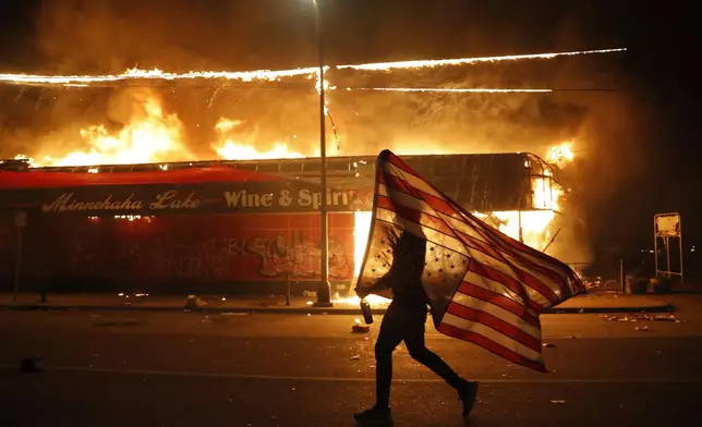 FILE - A protester carries a U.S. flag upside down, a sign of distress, next to a burning building on May 28, 2020, in Minneapolis. (AP Photo/Julio Cortez, File)