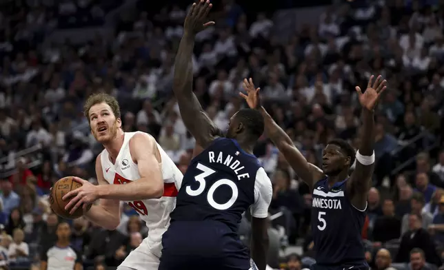 Toronto Raptors center Jakob Poeltl (19) drives toward the hoop while Minnesota Timberwolves forward Julius Randle (30) and guard Anthony Edwards (5) defend during the first half of an NBA basketball game, Saturday, Oct. 26, 2024, in Minneapolis. (AP Photo/Ellen Schmidt)