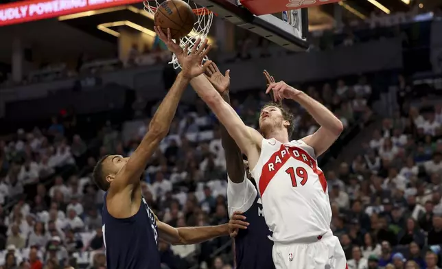 Toronto Raptors center Jakob Poeltl (19) shoots against Minnesota Timberwolves center Rudy Gobert, left, and forward Julius Randle, center, during the first half of an NBA basketball game, Saturday, Oct. 26, 2024, in Minneapolis. (AP Photo/Ellen Schmidt)