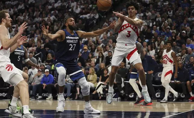 Toronto Raptors guard D.J. Carton (3) passes under the hoop while Minnesota Timberwolves center Rudy Gobert (27) defends during the first half of an NBA basketball game, Saturday, Oct. 26, 2024, in Minneapolis. (AP Photo/Ellen Schmidt)