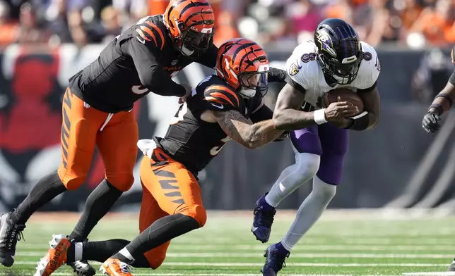 Baltimore Ravens quarterback Lamar Jackson=, right, runs with the ball as Cincinnati Bengals defensive end Trey Hendrickson, left, and linebacker Logan Wilson try to stop him during the second half of an NFL football game, Sunday, Oct. 6, 2024, in Cincinnati. (AP Photo/Carolyn Kaster)