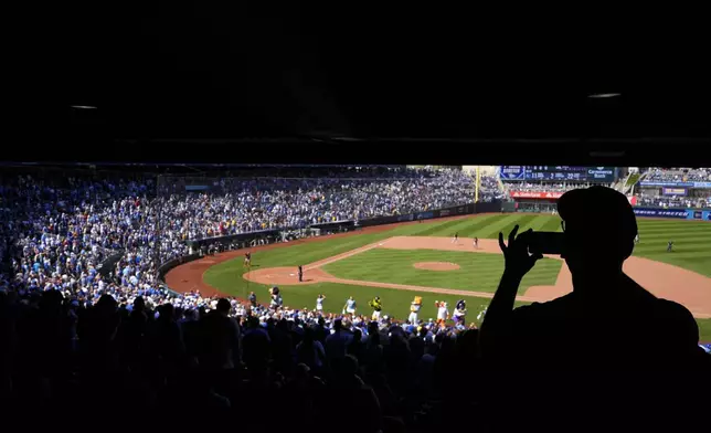 FILE - A fan takes photos during the seventh inning of a baseball game between the Minnesota Twins and the Kansas City Royals Sunday, Sept. 8, 2024, in Kansas City, Mo. (AP Photo/Charlie Riedel, File)