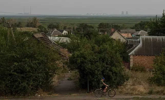 With the Zaporizhzhia nuclear power plant in the background, a bicyclist travels along a path in Nikopol, Ukraine, Sept. 2, 2024. Russian forces have controlled the plant since the first weeks of the war. (AP Photo/Evgeniy Maloletka)