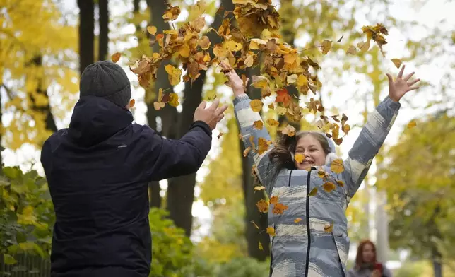 A man and a girl throw up fallen leaves in the Summer Garden in St. Petersburg, Russia, Wednesday, Oct. 16, 2024. (AP Photo/Dmitri Lovetsky)