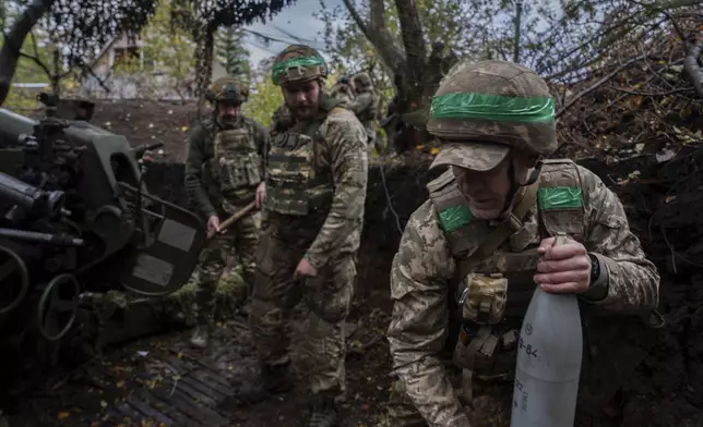 Ukrainian serviceman of Khartia brigade carries shell to the D-30 Howitzer in order to fire towards Russian positions in Kharkiv region, Ukraine, Wednesday, Oct. 16, 2024. (AP Photo/Alex Babenko)