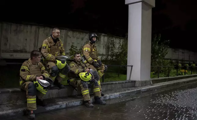 Firefighters rest on a curb during after responding to a Russian attack that killed a teenager in Kyiv, Ukraine, early Saturday, Oct. 26, 2024. (AP Photo/Alex Babenko)