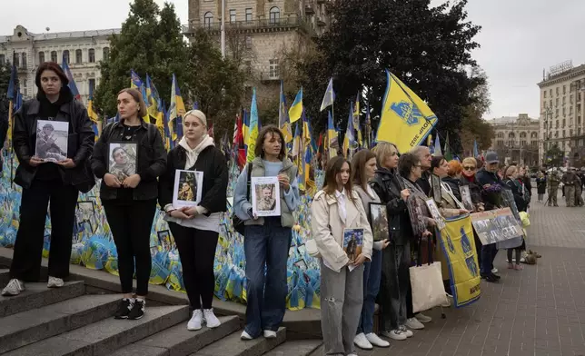 People hold photos of their relatives soldiers to keep a nationwide minute of silence in memory of fallen soldiers, who defended their homeland in war with Russia, on Defenders Day at the improvised war memorial in Independence square in Kyiv, Ukraine, Tuesday, Oct. 1, 2024. (AP Photo/Efrem Lukatsky)